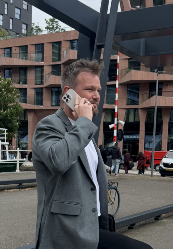 Man in a gray suit talking on a phone outdoors near modern buildings and a plaza