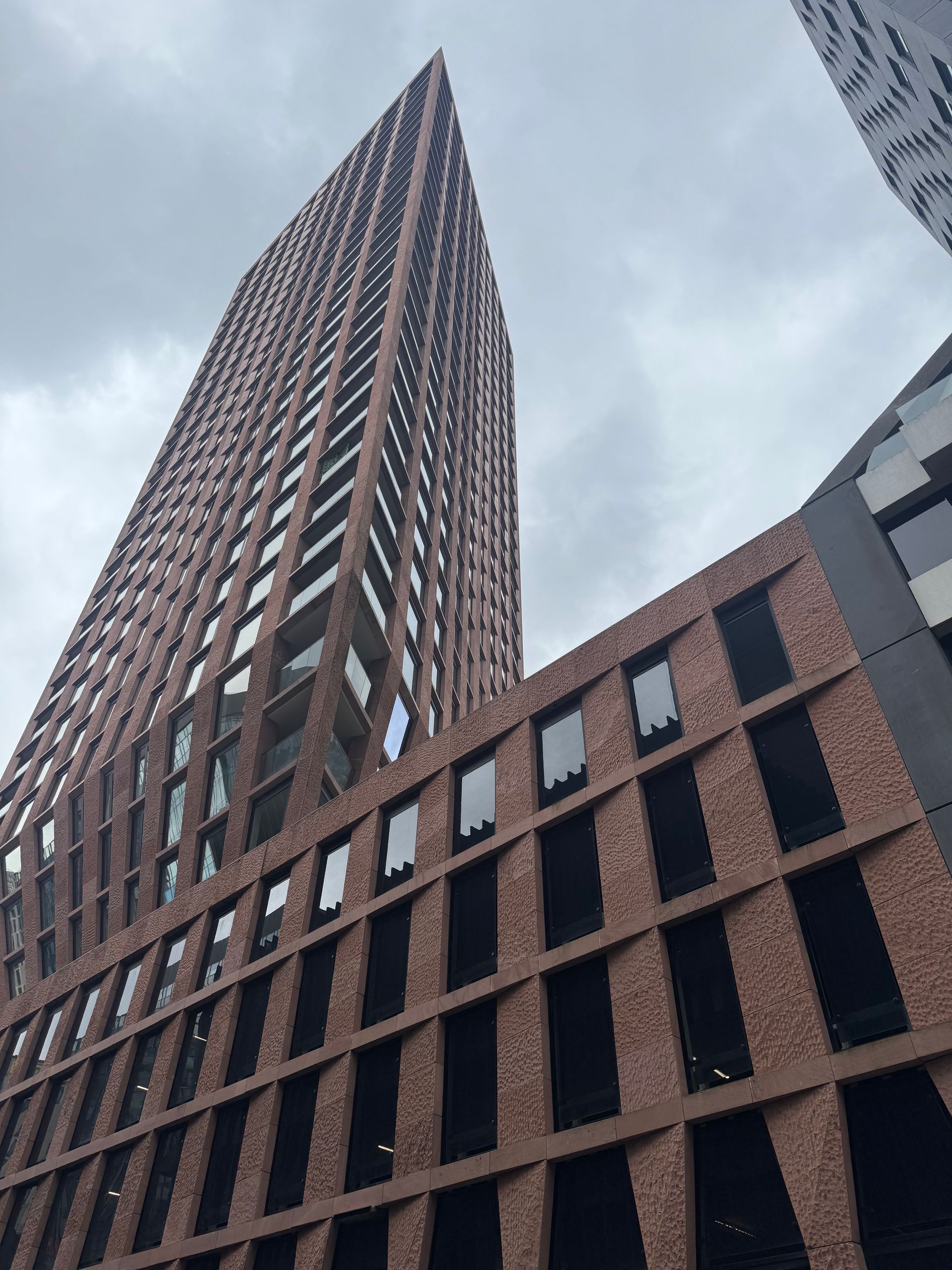 Low-angle view of a tall red-brick skyscraper against a cloudy sky