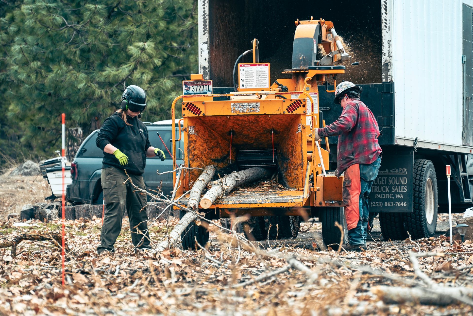 Two men are working on a wood chipper in a field.