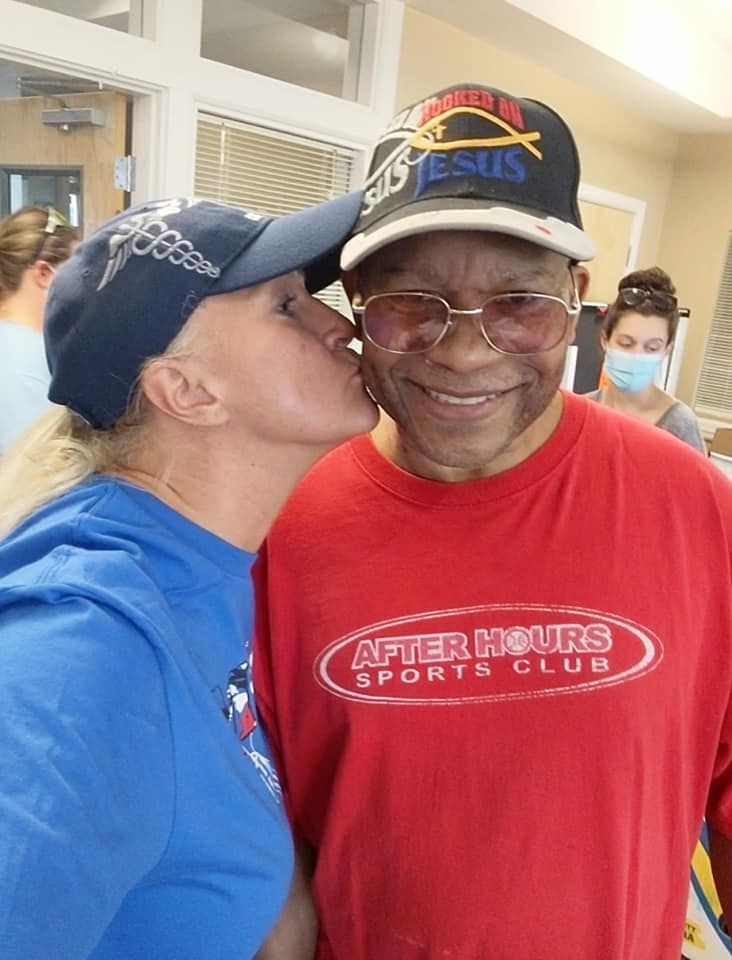 A woman kisses a man wearing a red shirt that says after hours sports club