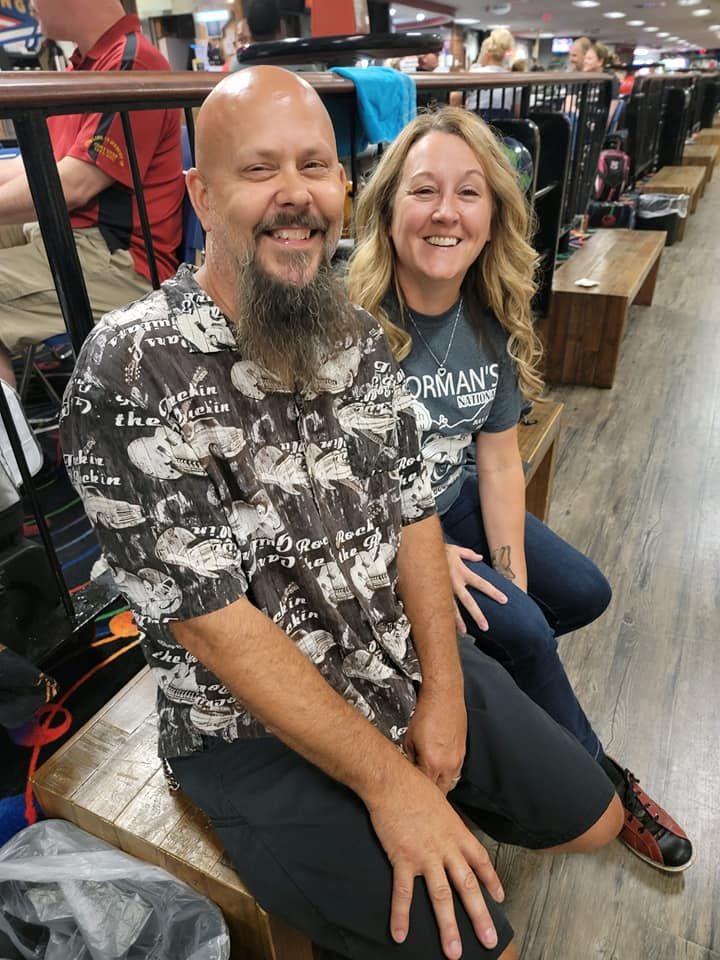 A man and a woman are sitting on a bench in a bowling alley.