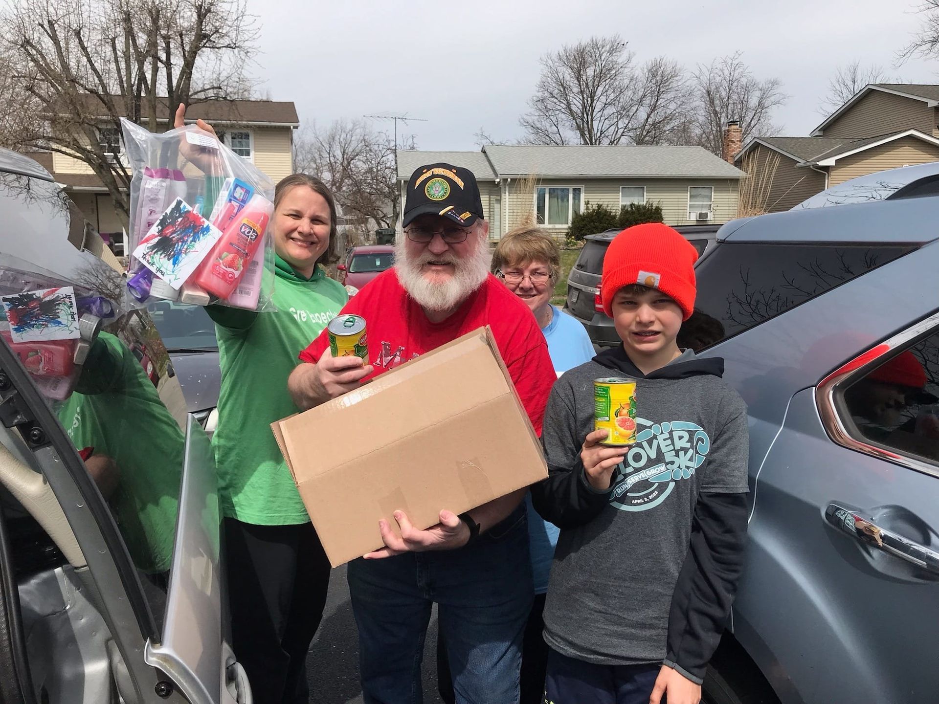 A group of people are standing in front of a car holding boxes.