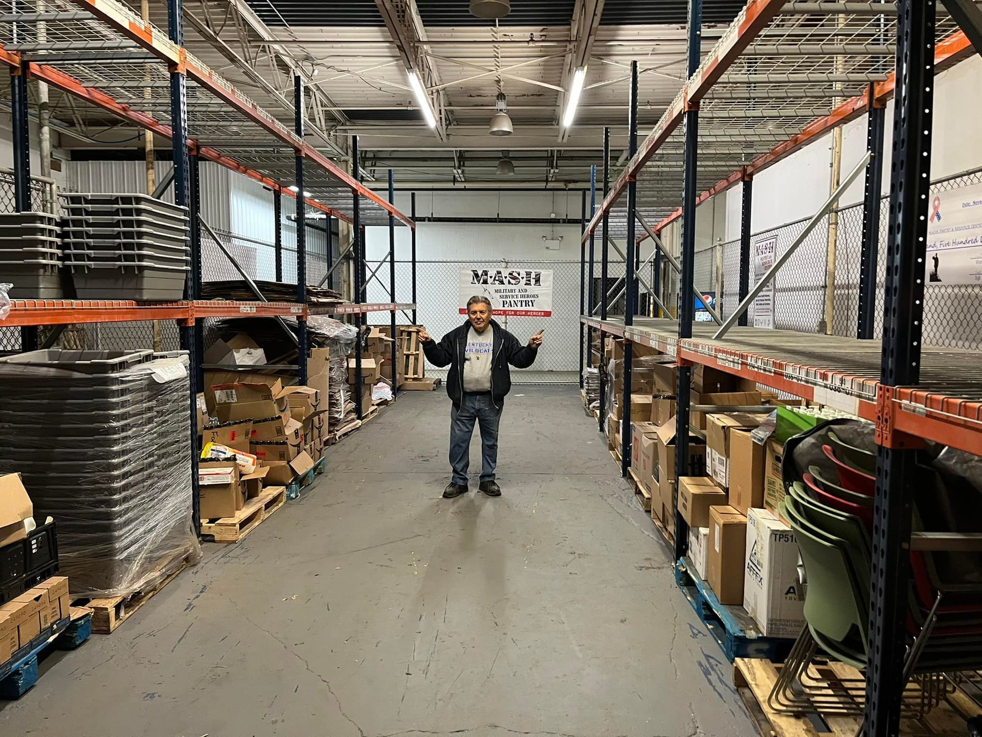 A man is standing in a warehouse filled with shelves and boxes.