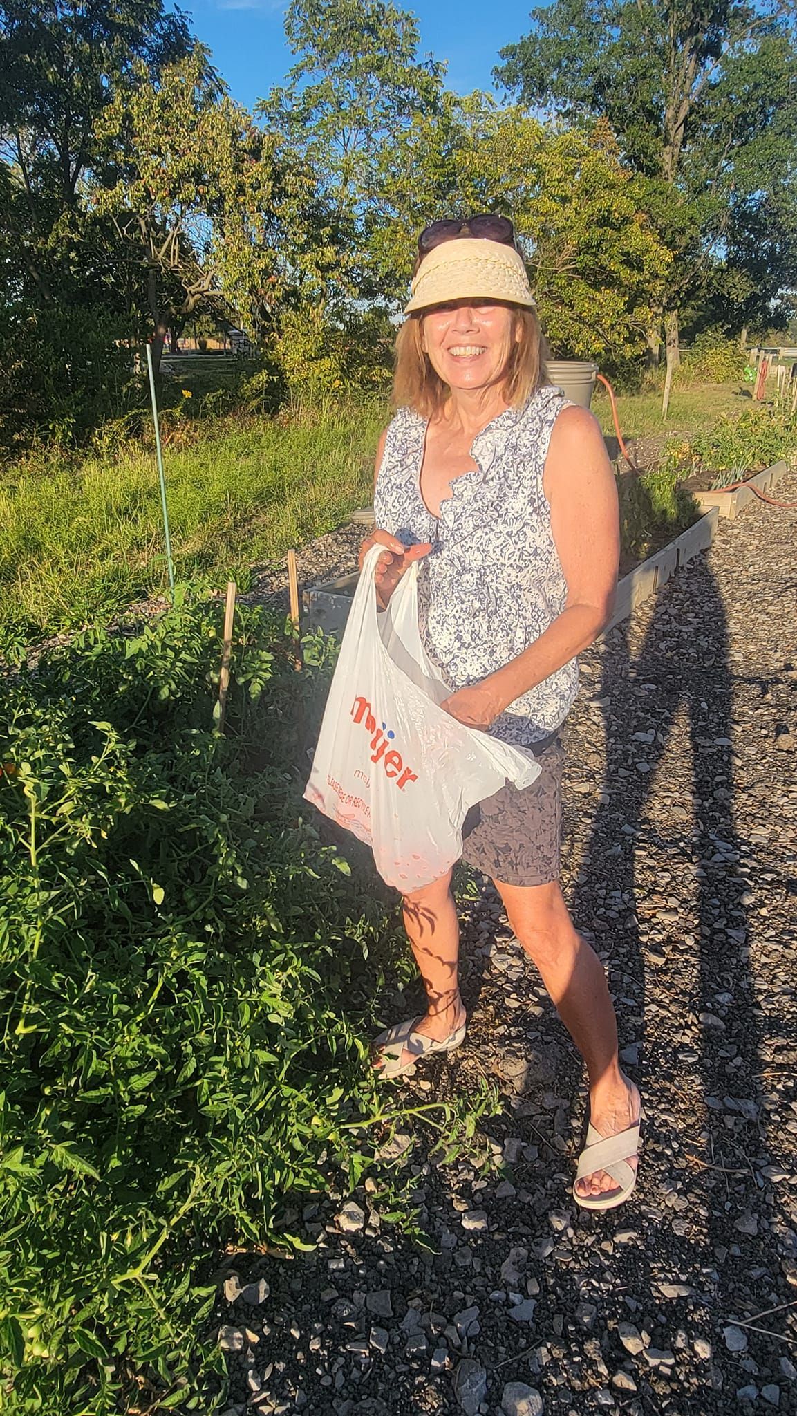 A woman is standing in a garden holding a white bag.