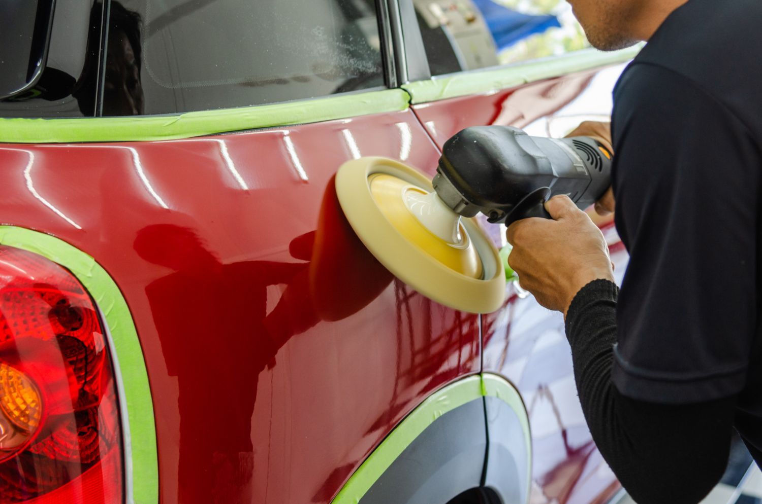 A man is polishing a red car with a polisher.
