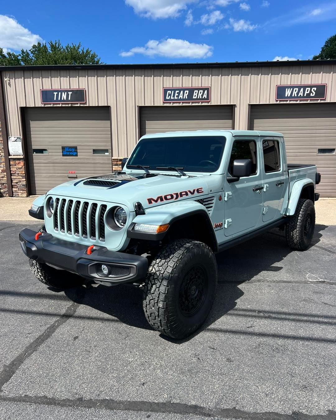 A white jeep gladiator is parked in front of a garage.