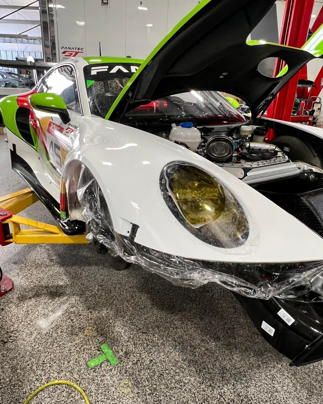 A green and white sports car with the hood up is being worked on in a garage.