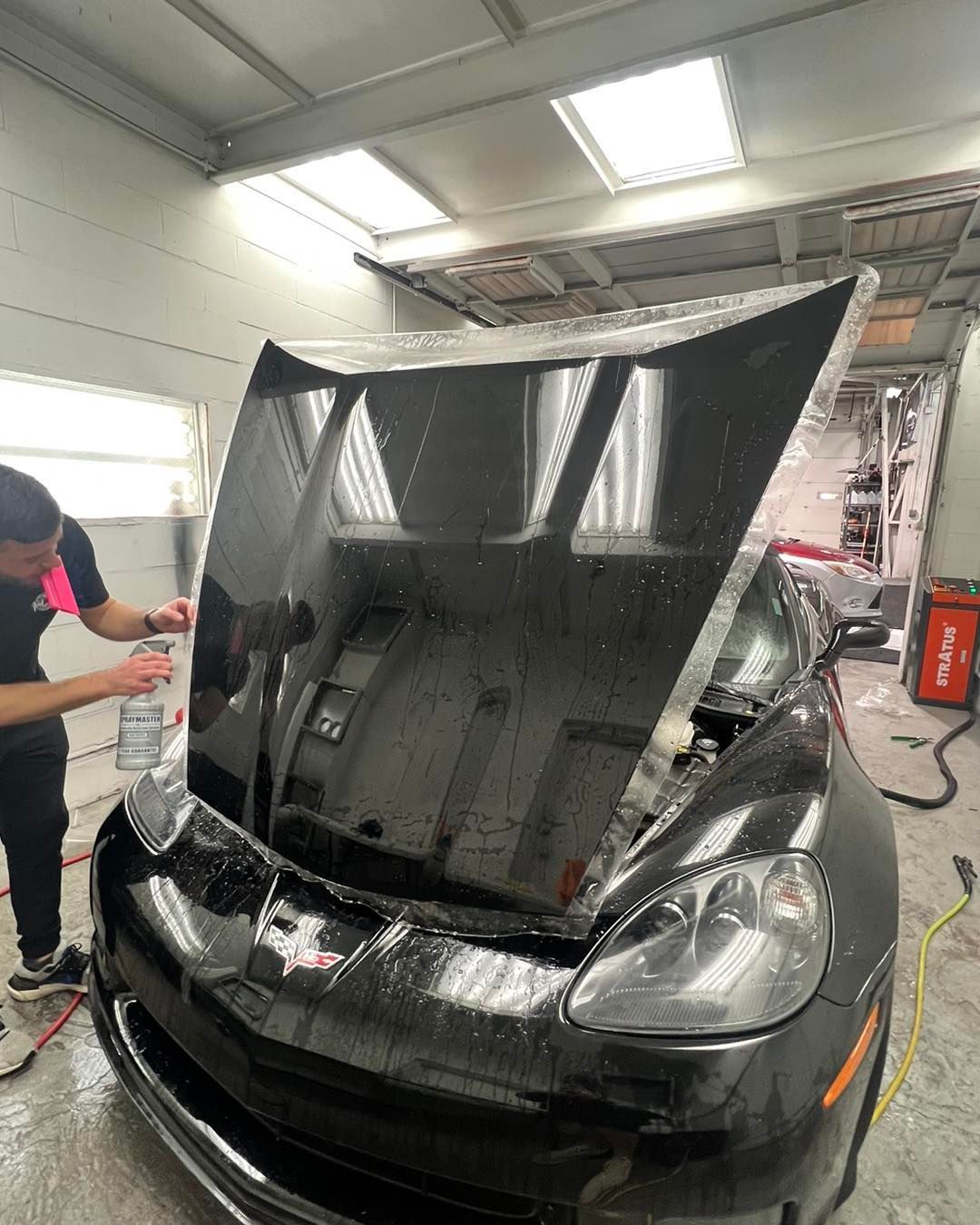 A man is cleaning the hood of a black car in a garage.