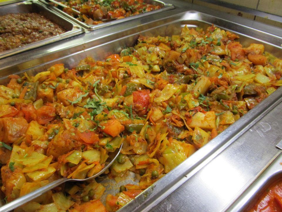 Catered food buffet with various vegetable dishes in metal trays.