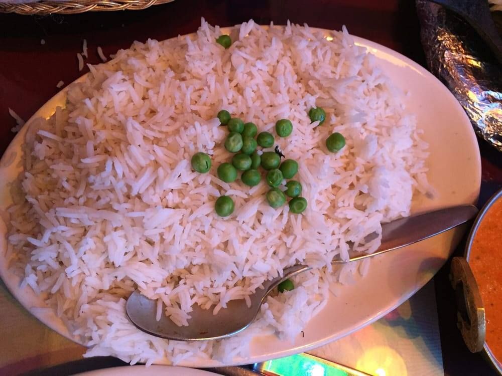 Plate of white rice with green peas, and a spoon and knife.