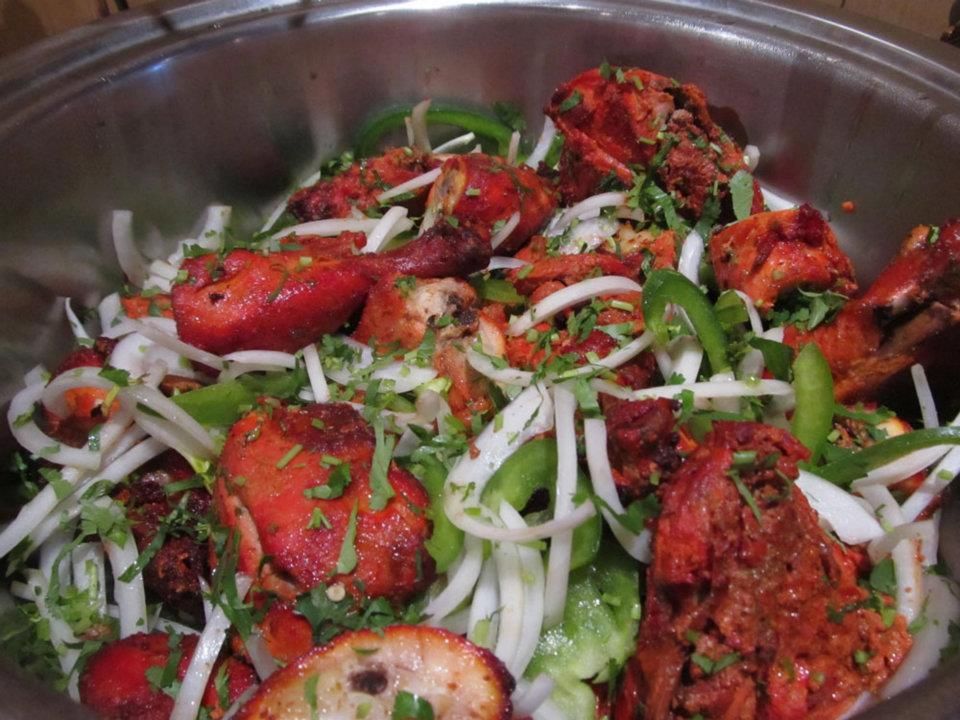Roasted red chicken pieces with onions, peppers, and herbs in a metal bowl.