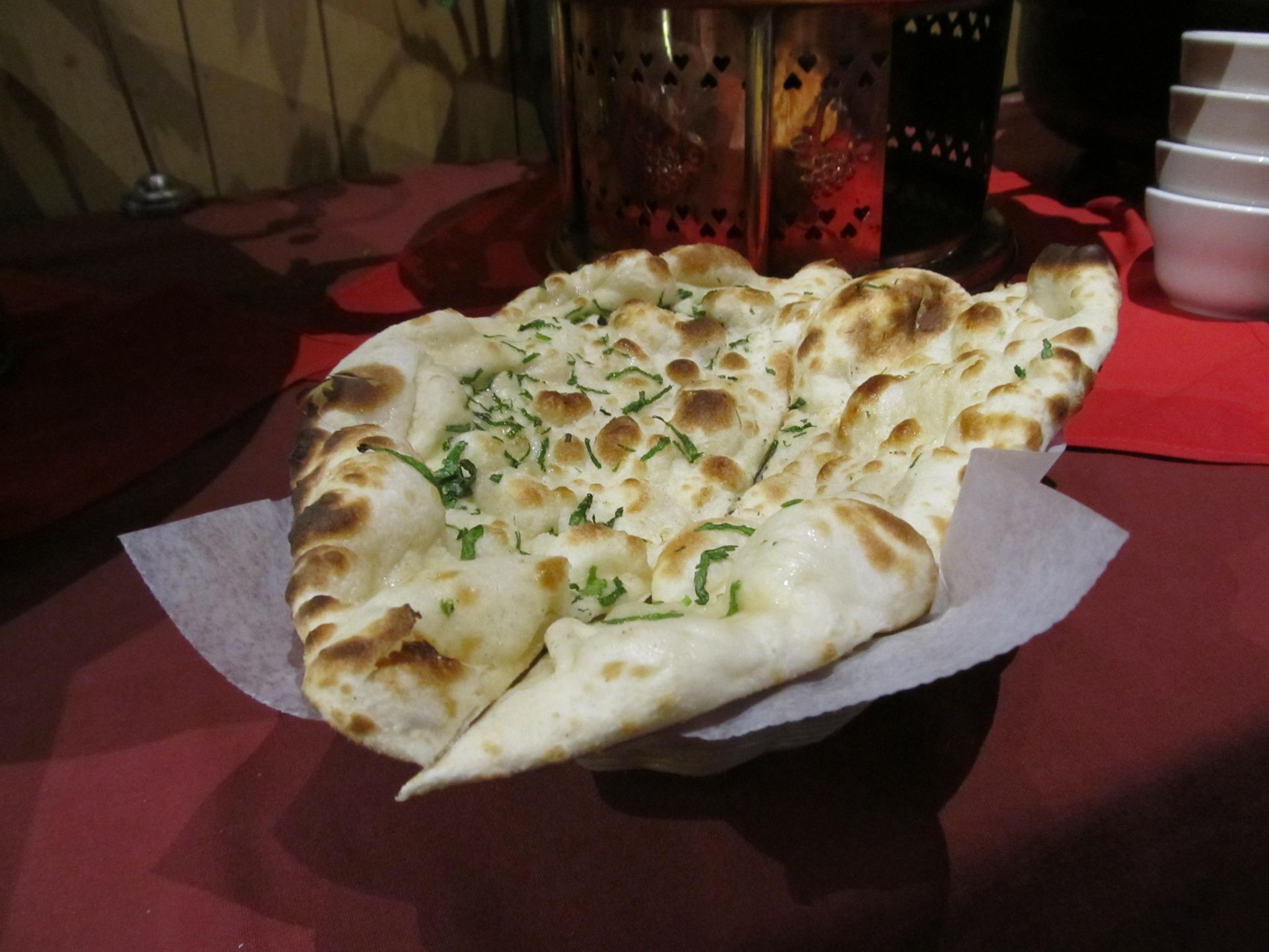 Naan bread sprinkled with herbs on a paper in a restaurant setting.