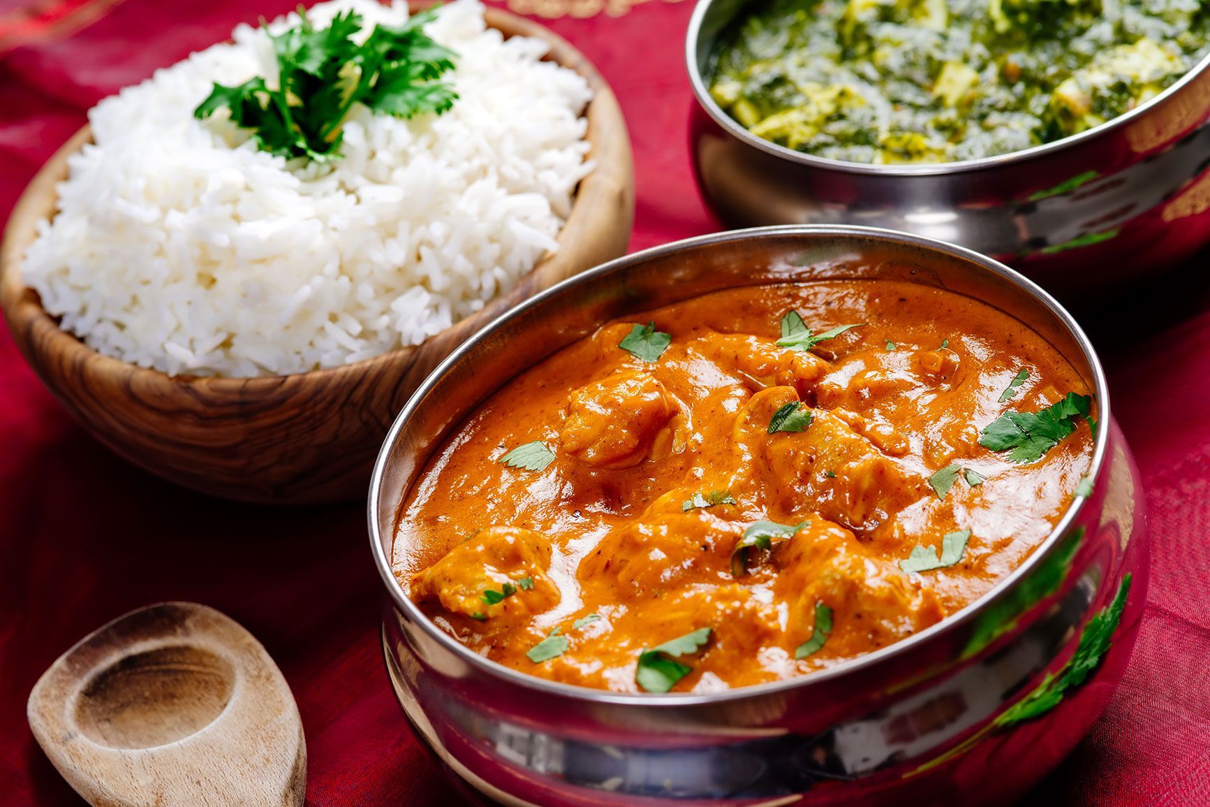 Indian dishes: butter chicken, palak paneer, rice in wooden bowl.