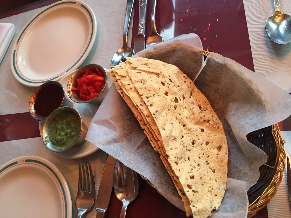 Table set with Indian food: basket of papadums, small bowls of chutney, and plates.