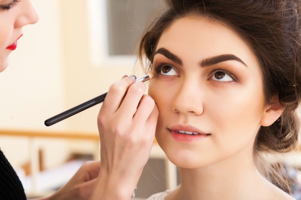 Makeup artist applying eyeshadow to a woman's eye with a brush; indoor setting. — Wow! Excellence in Hair in Toowoomba, QLD