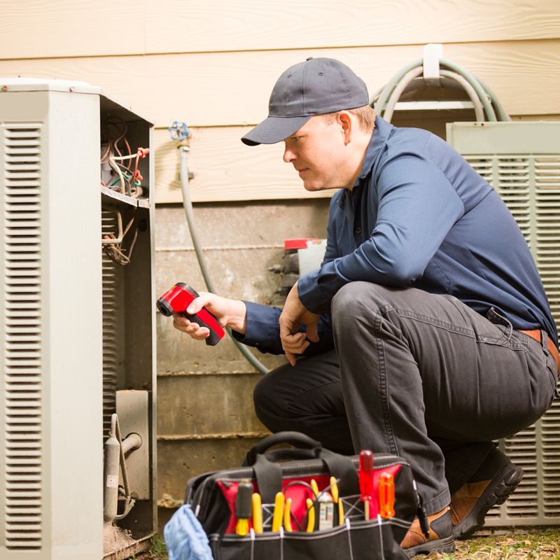 Technician kneeling beside an outdoor HVAC unit, checking wires with tools nearby