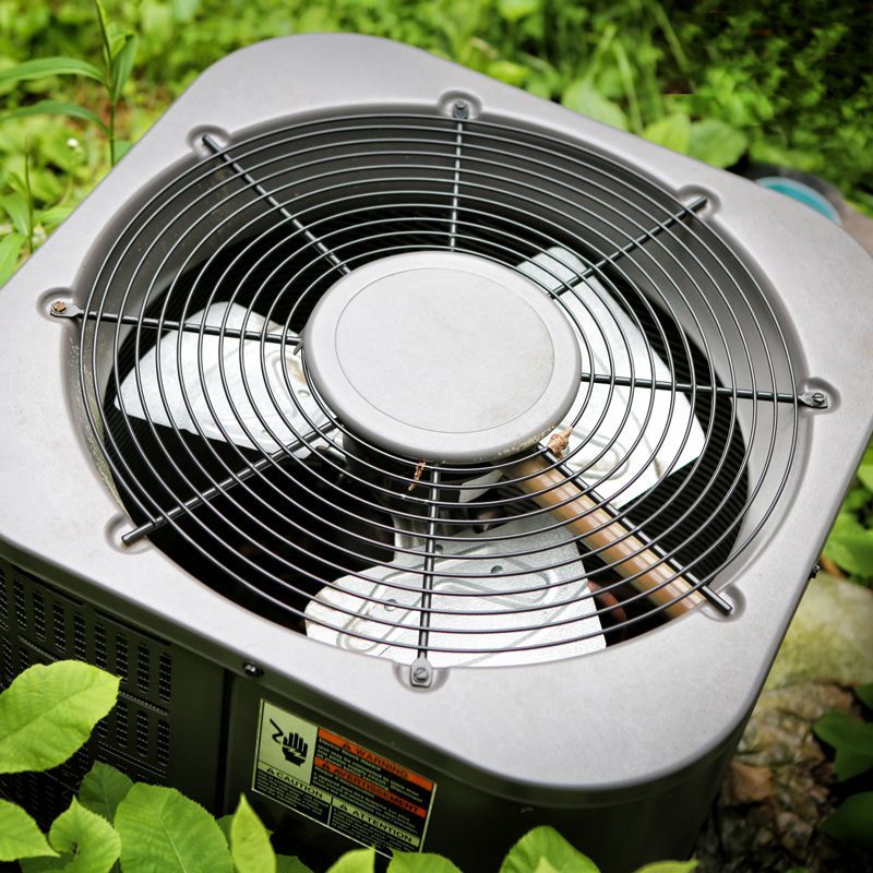 Close-up of a silver outdoor fan with a metal guard on grass and stones