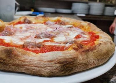 Primo piano di una pizza margherita a crosta spessa su un piatto bianco, con uno sfondo sfocato di una cucina.
