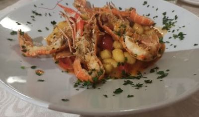 Pasta ai frutti di mare con gamberi ed erbe aromatiche su un piatto bianco.