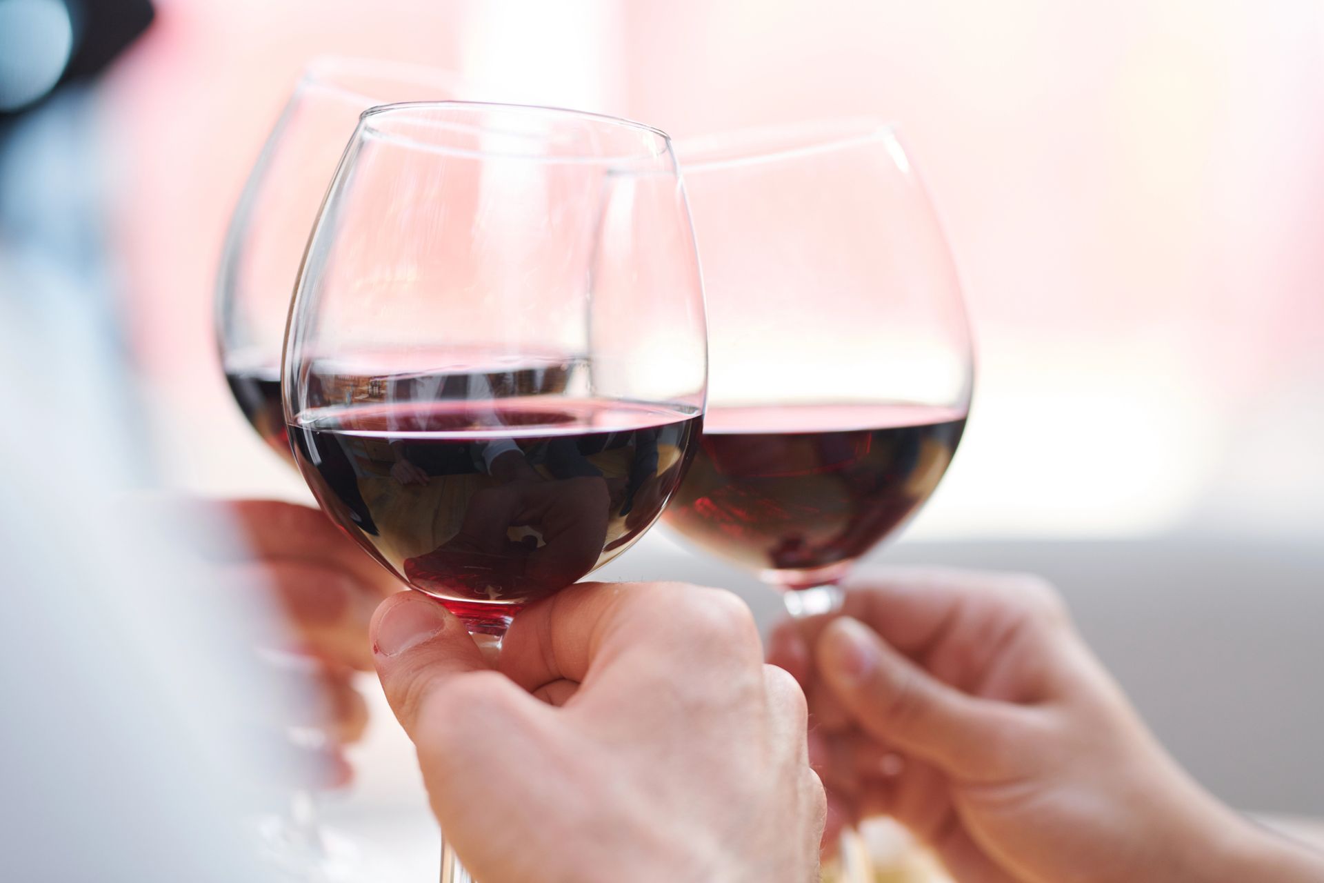 Due mani che brindano con calici di vino rosso in un ambiente illuminato da luci soffuse.