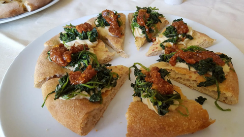 Fette di pane piatto condite con erbe aromatiche e salsa su un piatto bianco.