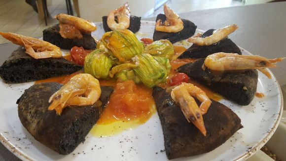 Antipasto di frutti di mare su un piatto bianco con fette di pane nero, gamberi e guarnizione di salsa gialla.