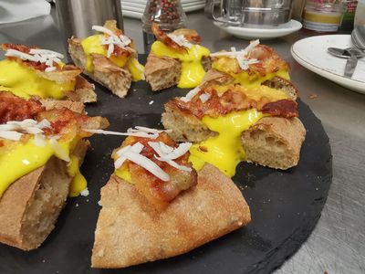 Fette di pizza con formaggio fuso e condimenti su un vassoio nero.