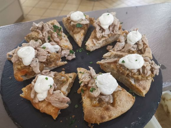 Piatto di focaccia a fette condita con carne sfilacciata e cucchiaiate di salsa bianca.