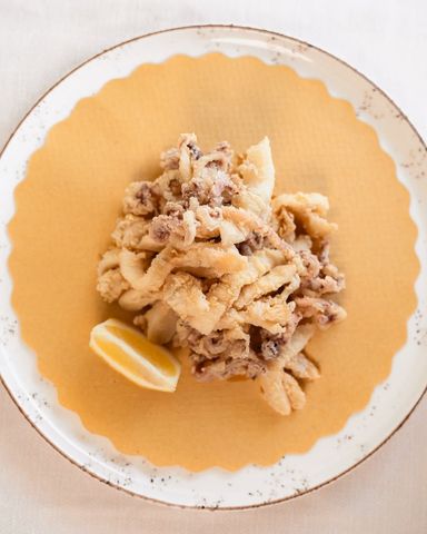 Pasta al sugo con uno spicchio di limone su un piatto giallo.