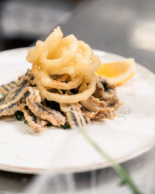 Calamari fritti con anelli di cipolla e spicchio di limone su un piatto bianco.