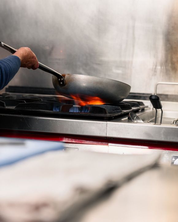 Lo chef mescola un wok in fiamme su un fornello in cucina