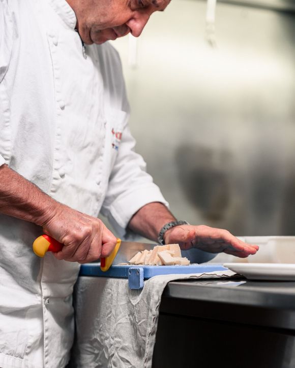 Uno chef in uniforme bianca affetta il cibo su un tagliere in cucina.