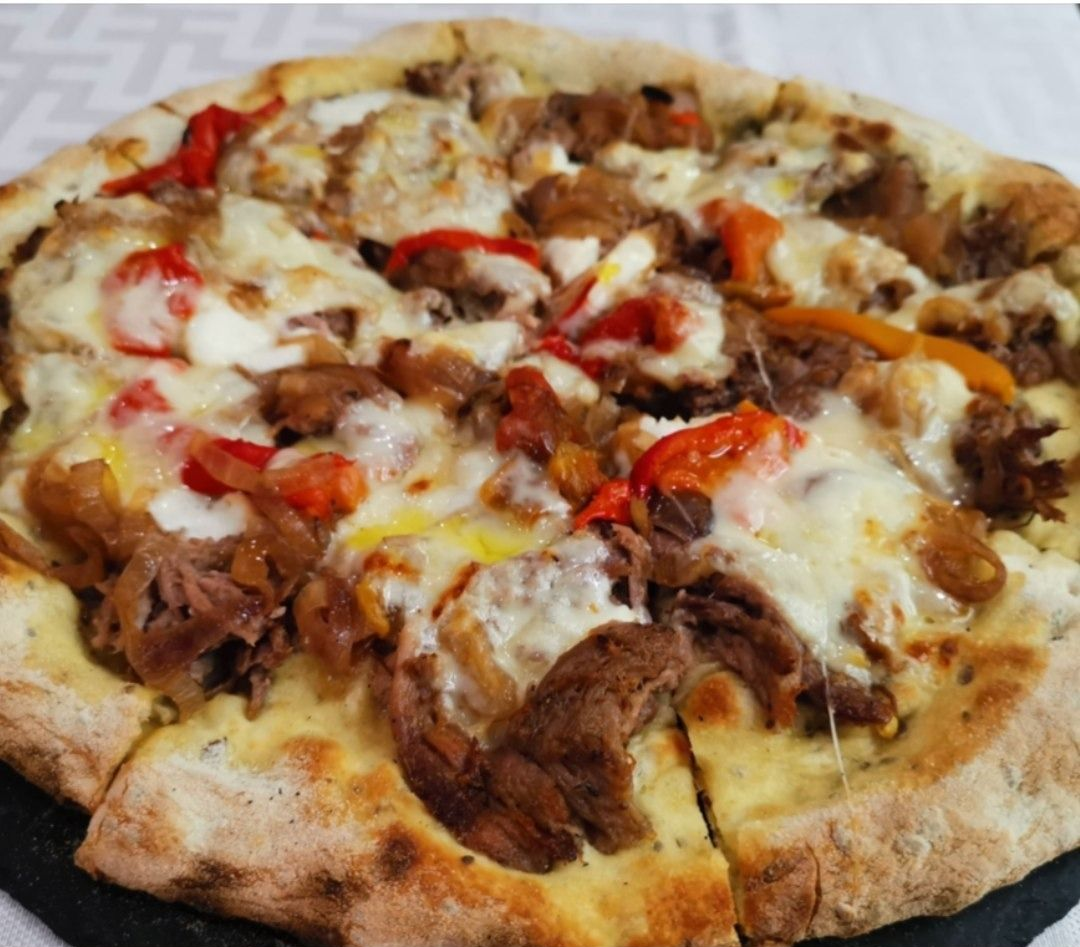 Primo piano di una pizza fatta in casa condita con formaggio fuso, peperoni arrostiti e carne su una superficie di legno.