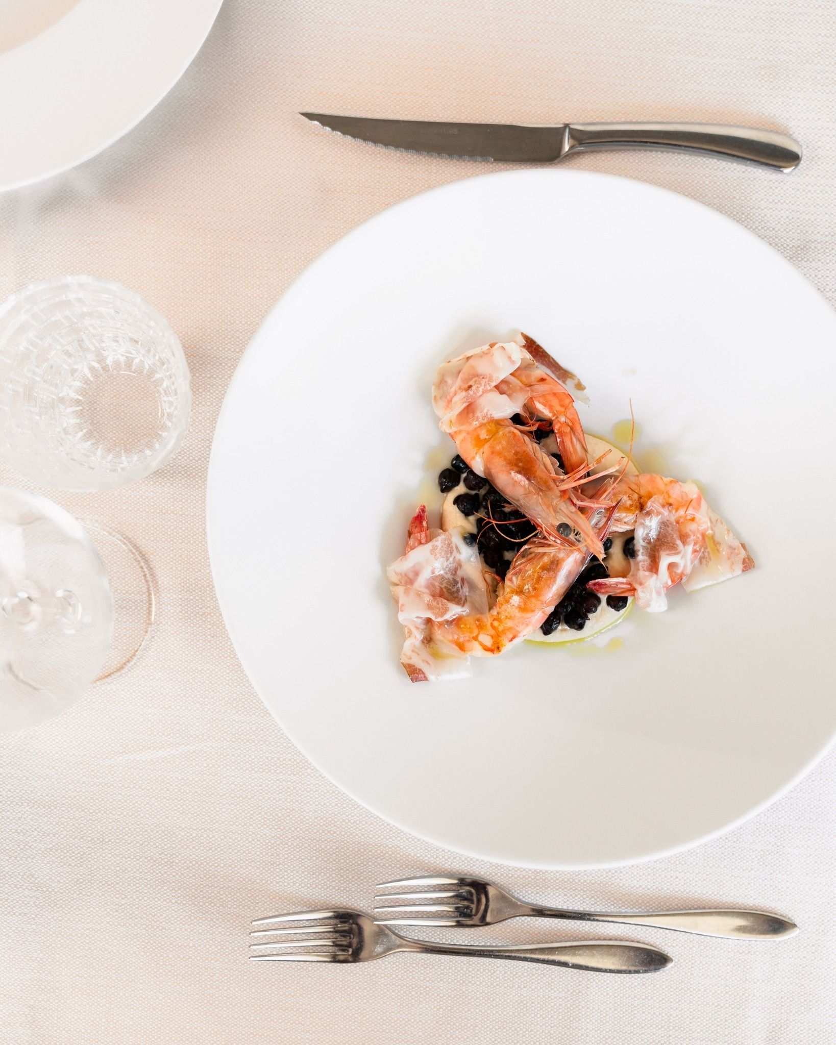 Piatto bianco con una piccola porzione di salmone su una tavola apparecchiata in modo leggero, con posate nelle vicinanze.