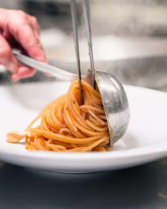 La pasta viene impiattata con pinze e cucchiaio su un piatto bianco.