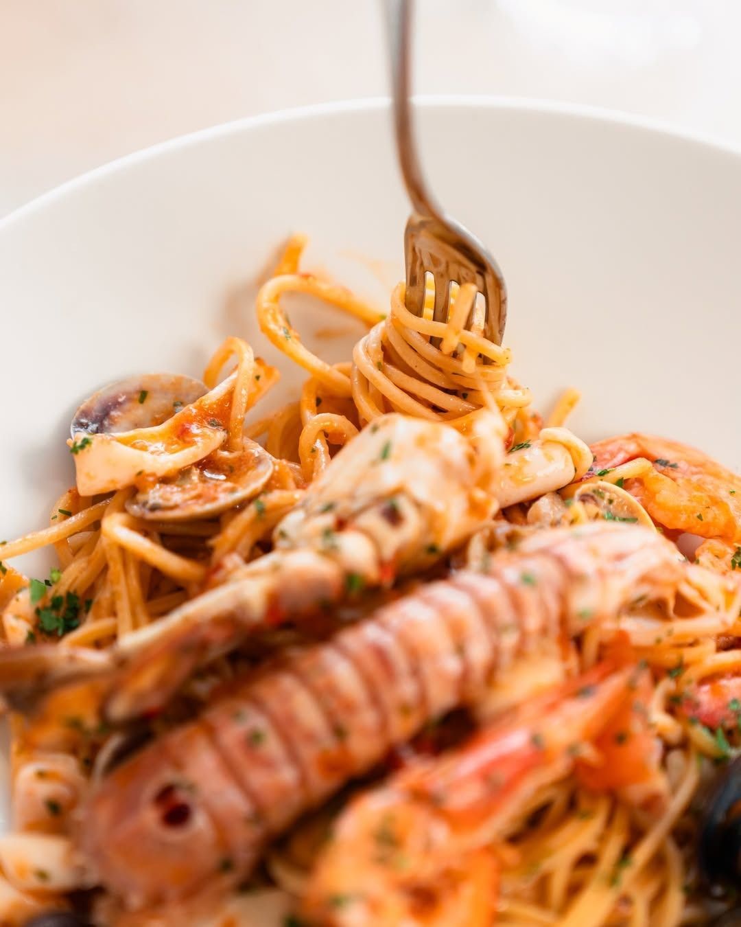 Primo piano di pasta ai frutti di mare con gamberi e cozze in una ciotola bianca, con una forchetta che arrotola gli spaghetti.