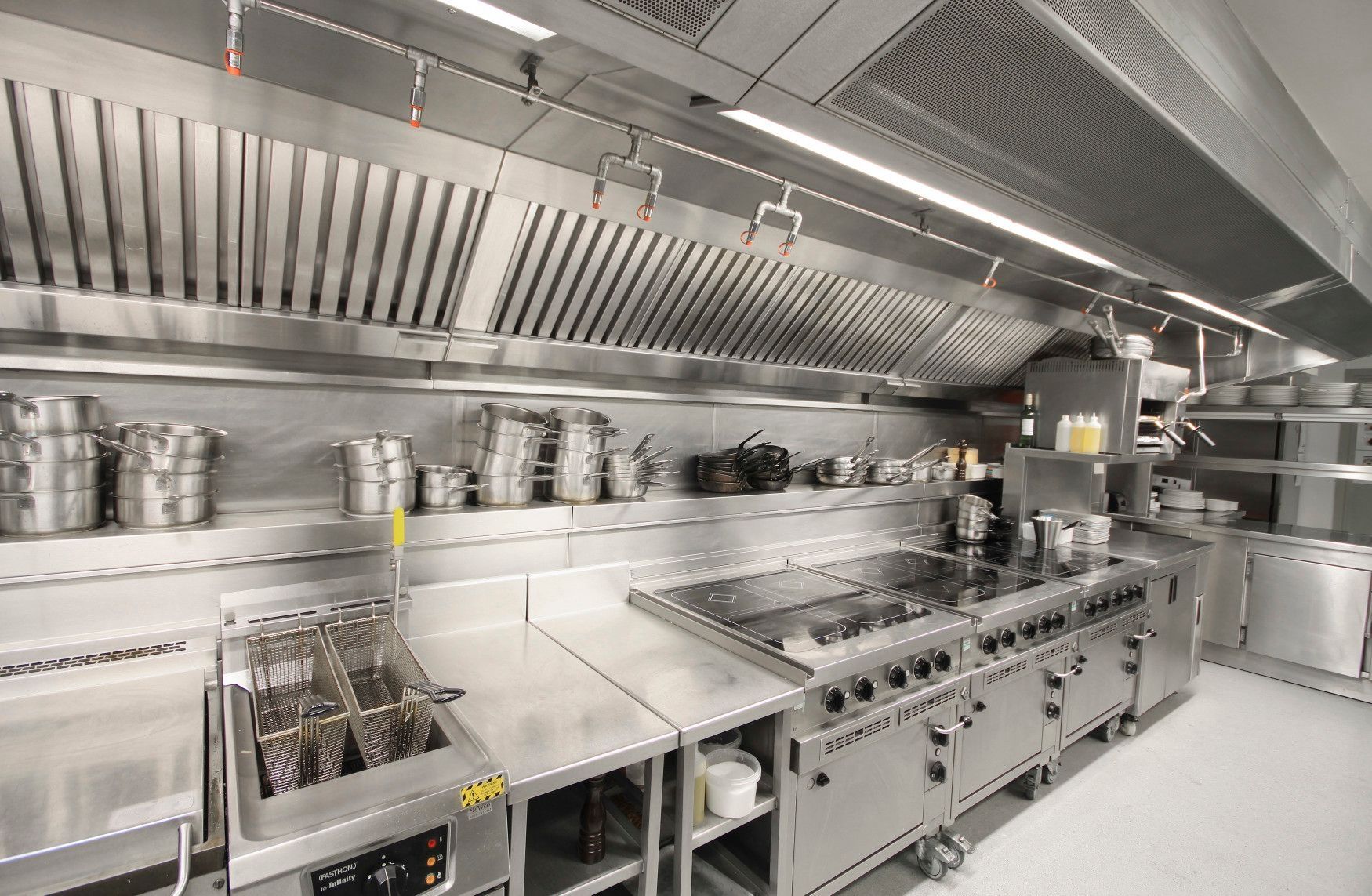 Commercial kitchen with stainless steel appliances, range, pots, oven, and hanging utensils.