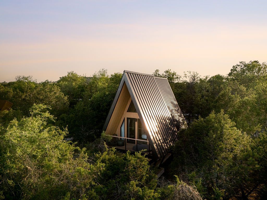 A-frame cabin nestled in dense green trees at sunset