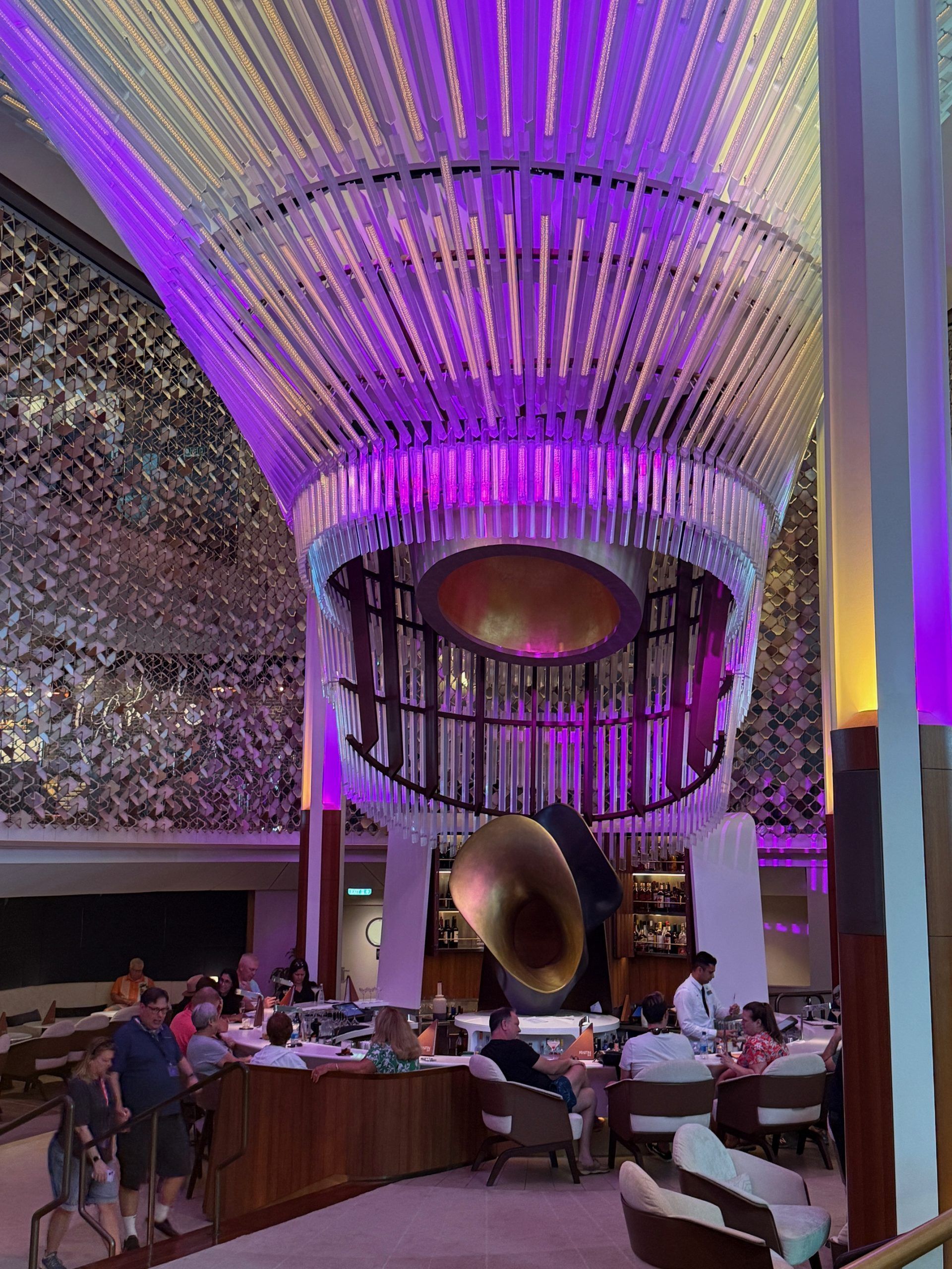 Purple-lit modern restaurant with a high curved ceiling, diners seated at tables, and a large circular hanging sculpture