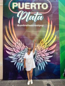 Woman posing in front of a colorful Puerto Plata mural with large pink, purple, and yellow wings