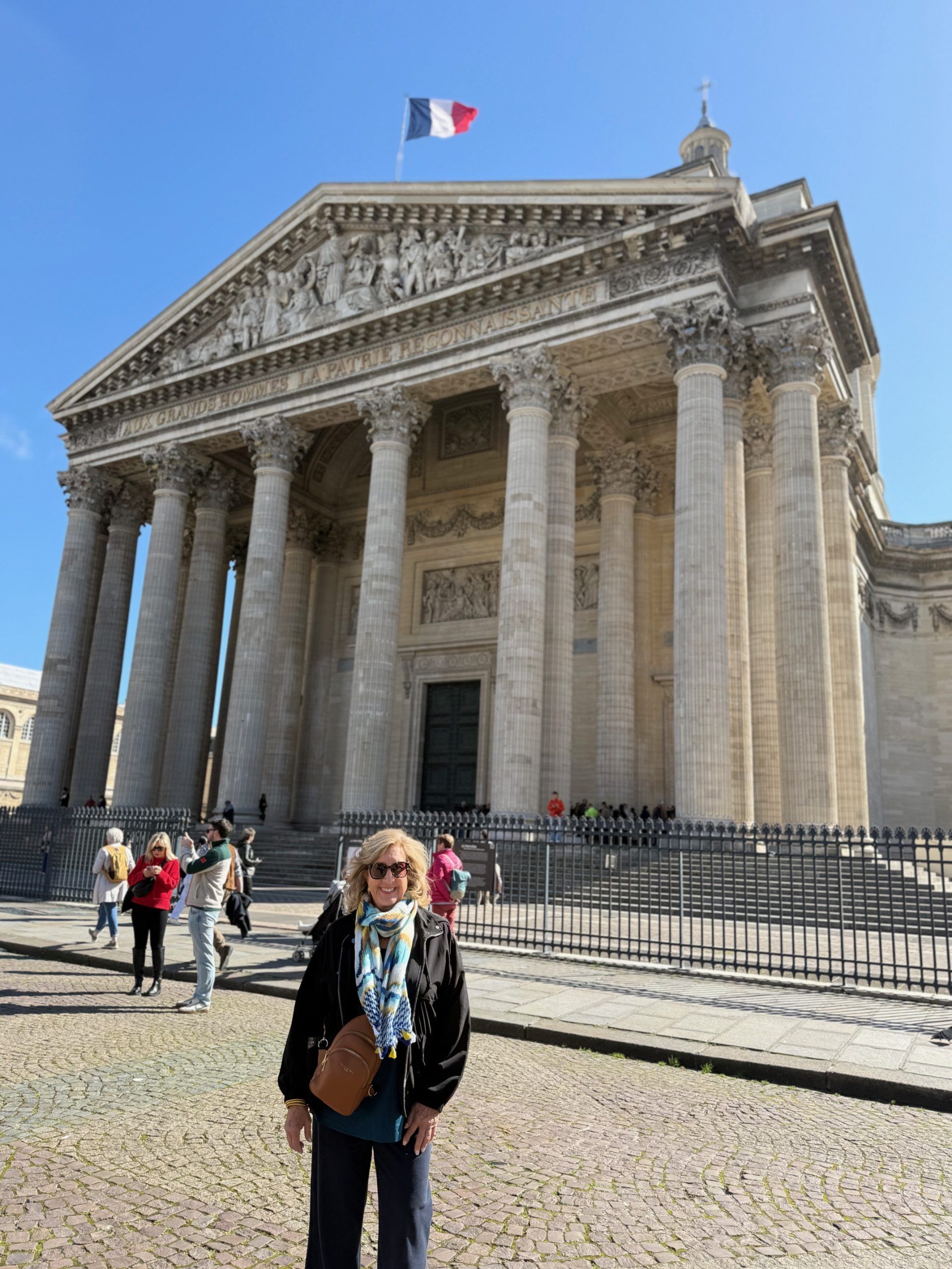 French parliament building with large columns and a French flag, with tourists walking in front