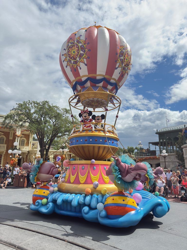 Colorful parade float with a striped hot air balloon and blue elephant figures on a theme park street