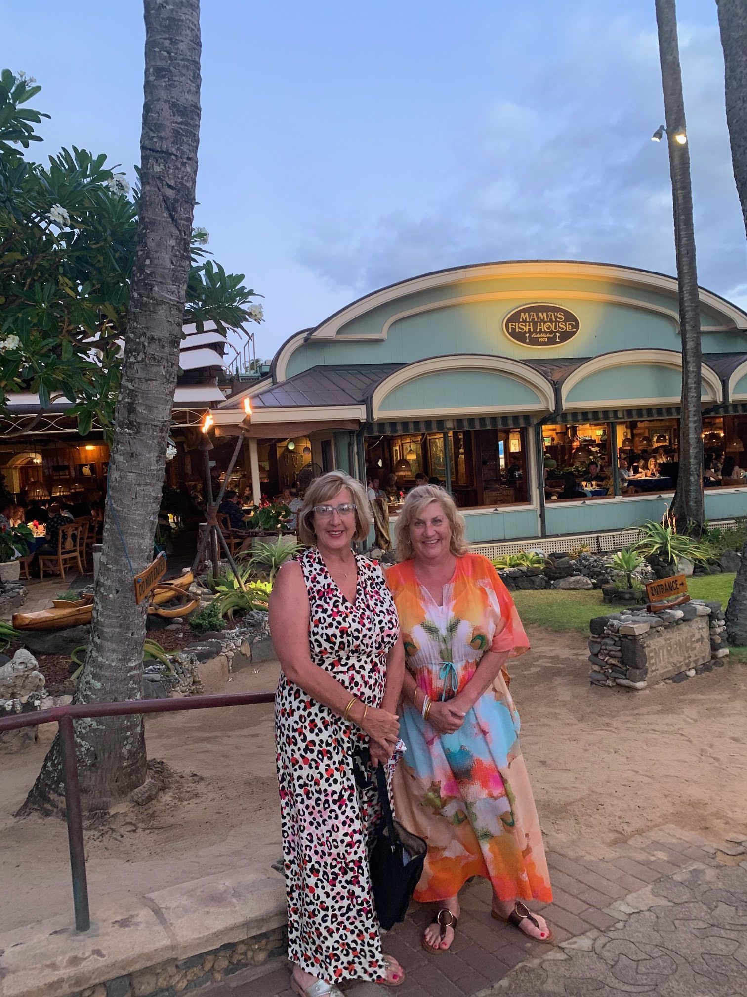 Two women posing in colorful outfits outside a lit building at dusk