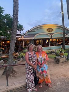 Two women standing together outdoors at dusk in front of a lit restaurant and palm trees