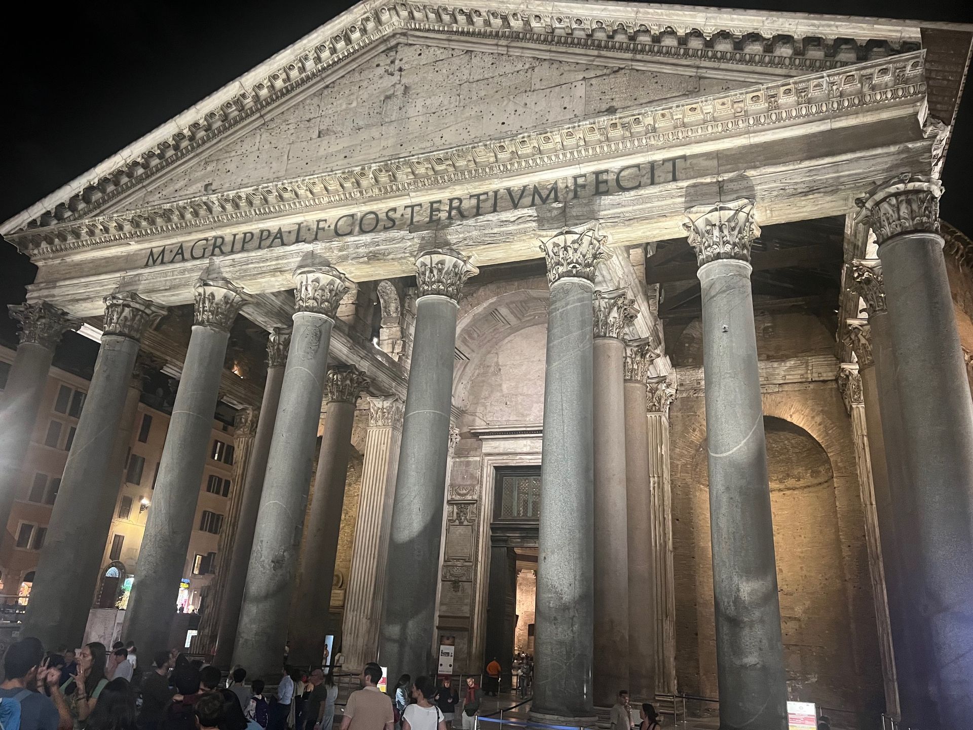 Illuminated ancient temple facade with tall columns and crowd of visitors at night