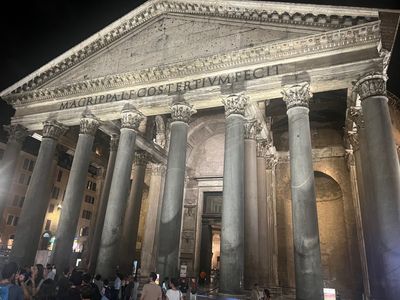 Illuminated ancient Roman temple façade with tall stone columns at night, crowds gathered below