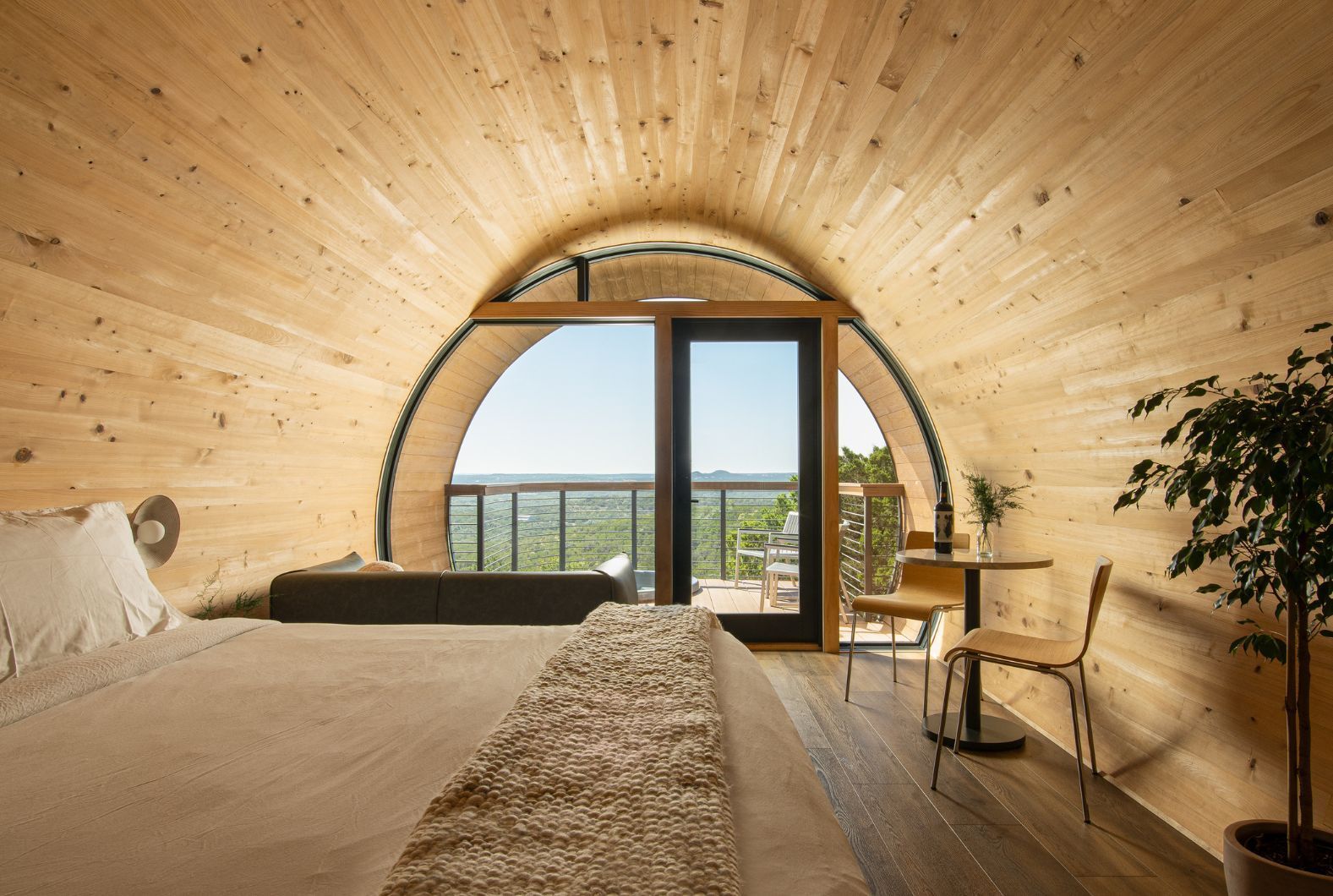 Minimalist arched wood bedroom with bed, desk, chair, and glass doors overlooking a city view