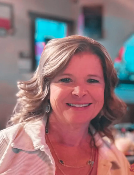 Smiling woman in a pink top, seated indoors with a blurred colorful background