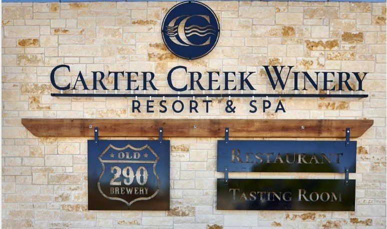 Carter Creek Winery Resort & Spa sign on a stone wall, with tasting room and Old 290 Brewery signs beneath it