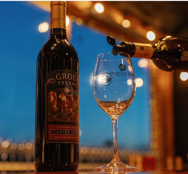 Wine bottle and stemmed glass on a table with warm string lights at dusk.